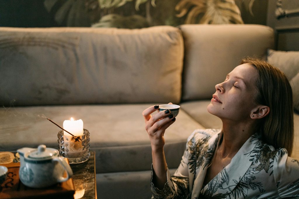 Woman relaxing at home and smelling a candle to calm her nervous system and reduce stress naturally.