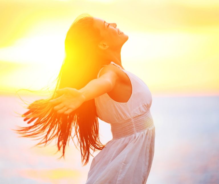 Woman standing outdoors with arms raised, symbolising freedom, recovery, and relief from burnout.