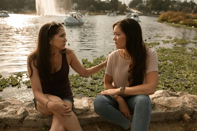 Two women sitting together confiding and supporting each other through emotional stress and nervous system overwhelm.