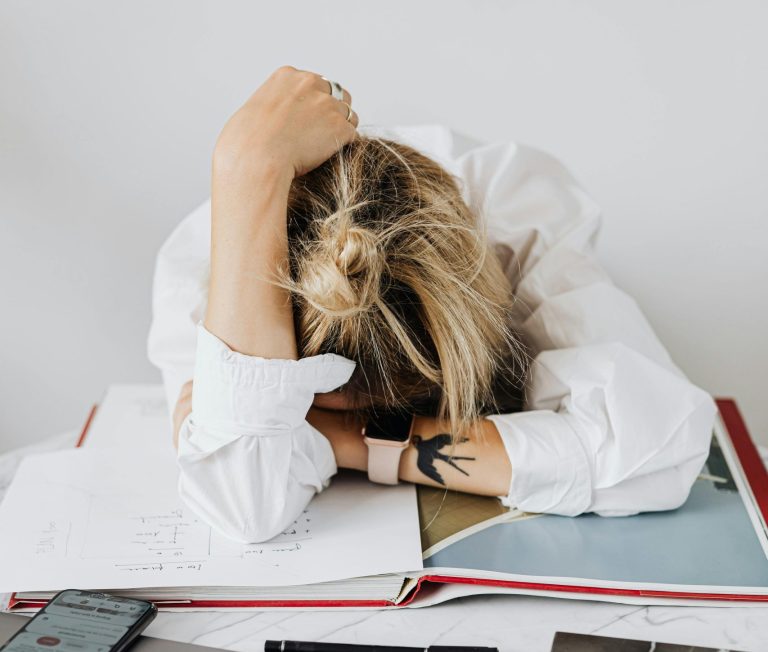 Woman resting her head on her desk, exhausted, highlighting chronic fatigue and emotional burnout in high-achieving women.